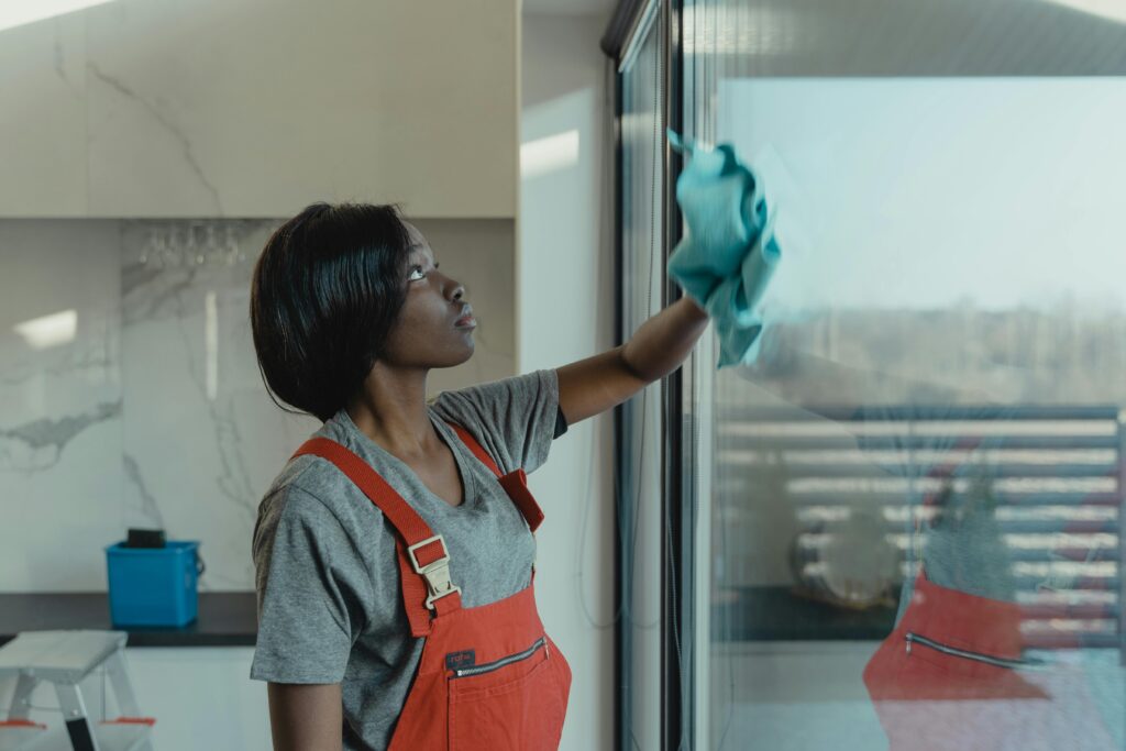 pexels-photo-6200808-6200808 A woman in overalls cleans a glass window with a rag, emphasizing professional housekeeping.